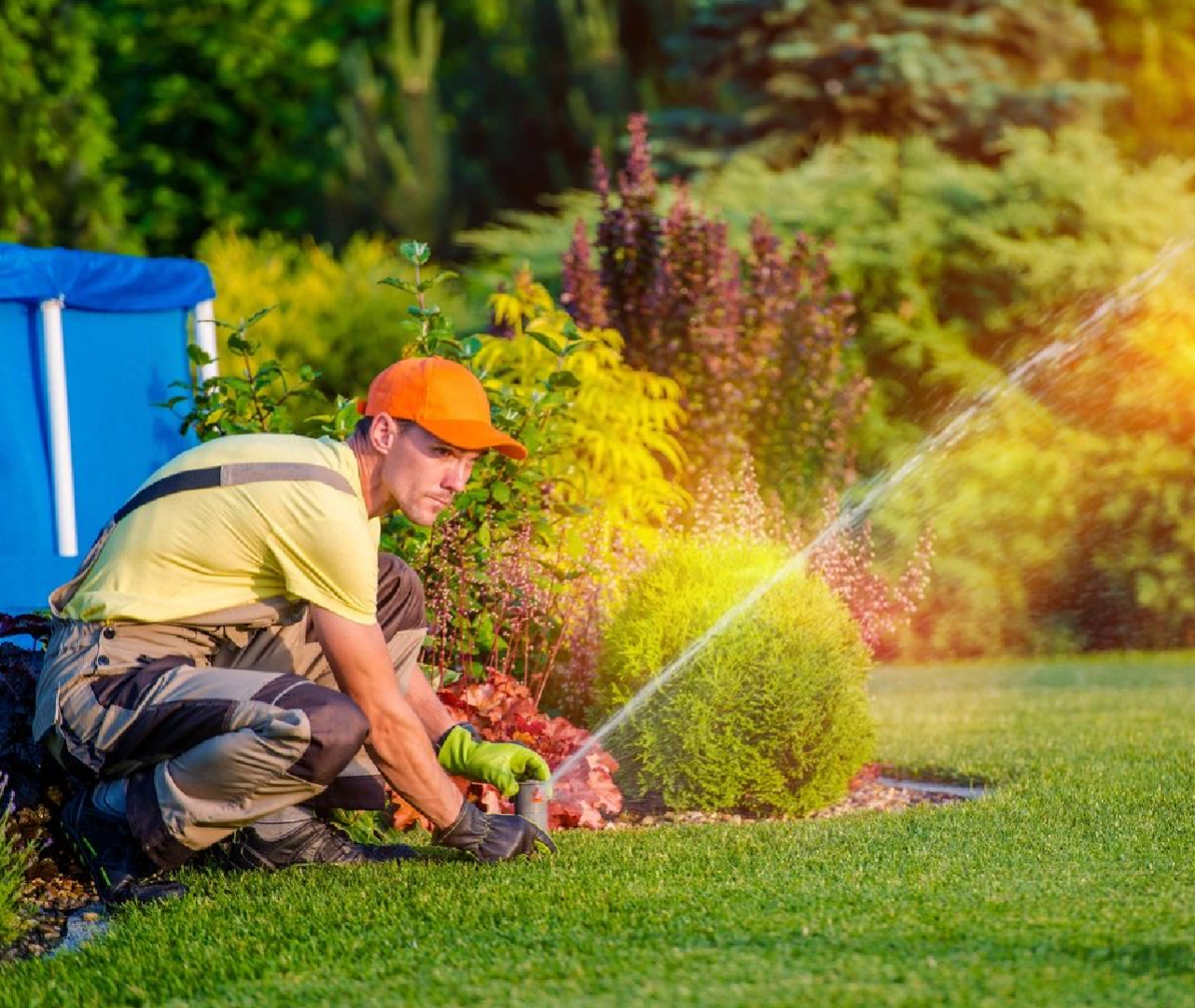 A man in yellow shirt and hat watering grass.