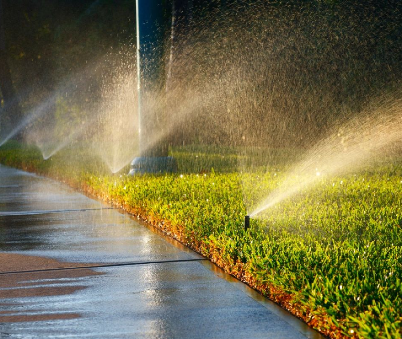 A couple of water sprinklers spraying on some grass.